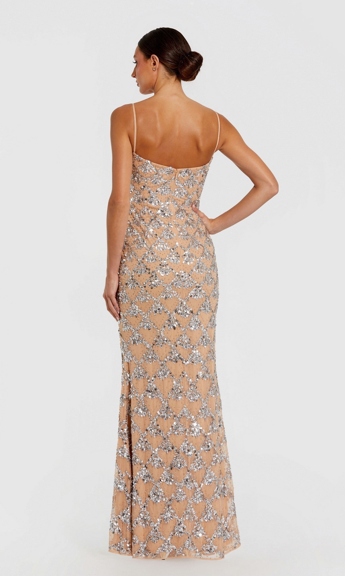 A woman stands facing away, wearing the Mac Duggal 94184 long formal dress—a floor-length, sleeveless gown with thin straps and a shimmering silver sequin geometric pattern over nude fabric.